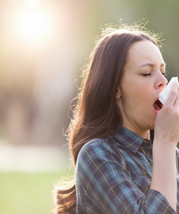 Woman sneezing in park with flowers in other hand طب سوزنی تسکین دهنده علائم آلرژی