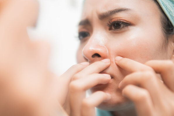 asian woman squeezing pimple on the cheek to the mirror